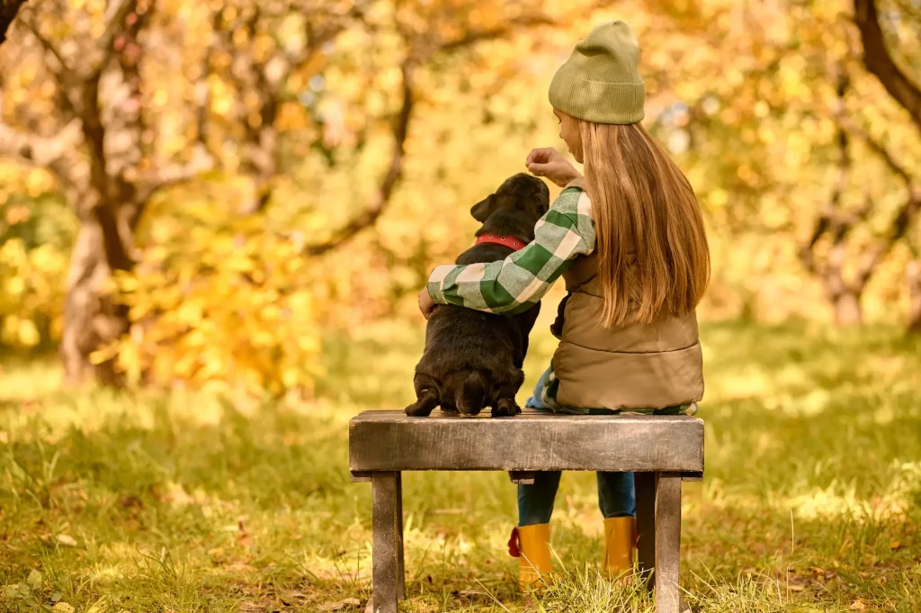 une petite fille blonde assise sur un banc dans les bois avec son chien lui donnant une friandise